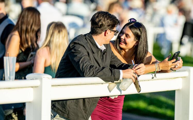 A couple smiling at the track side, enjoying a day at the races